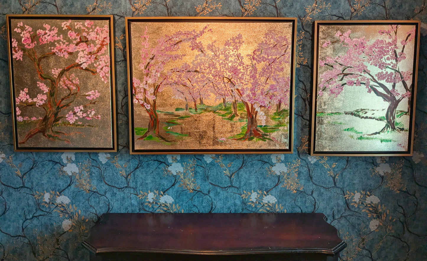 Three framed artworks of cherry blossom trees on a textured blue wall.